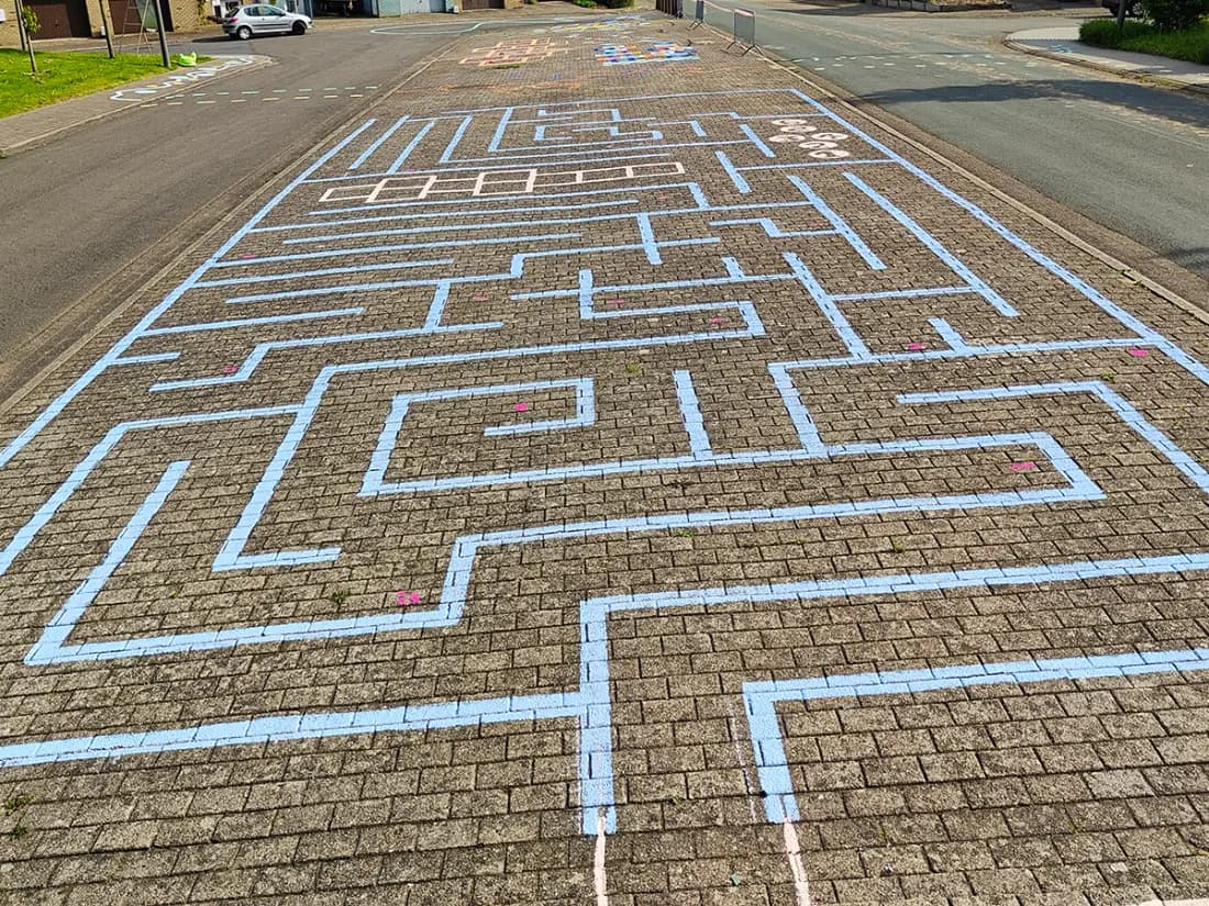 Een doolhof van lichtblauwe lijnen over de volle breedte van de straat. Verderop de hinkelvakken en het ronde speelveld.